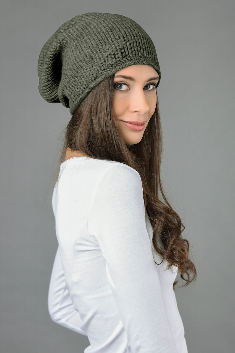 May include: A woman wearing a dark green slouchy beanie hat with a ribbed texture. She is wearing a white long-sleeved shirt.