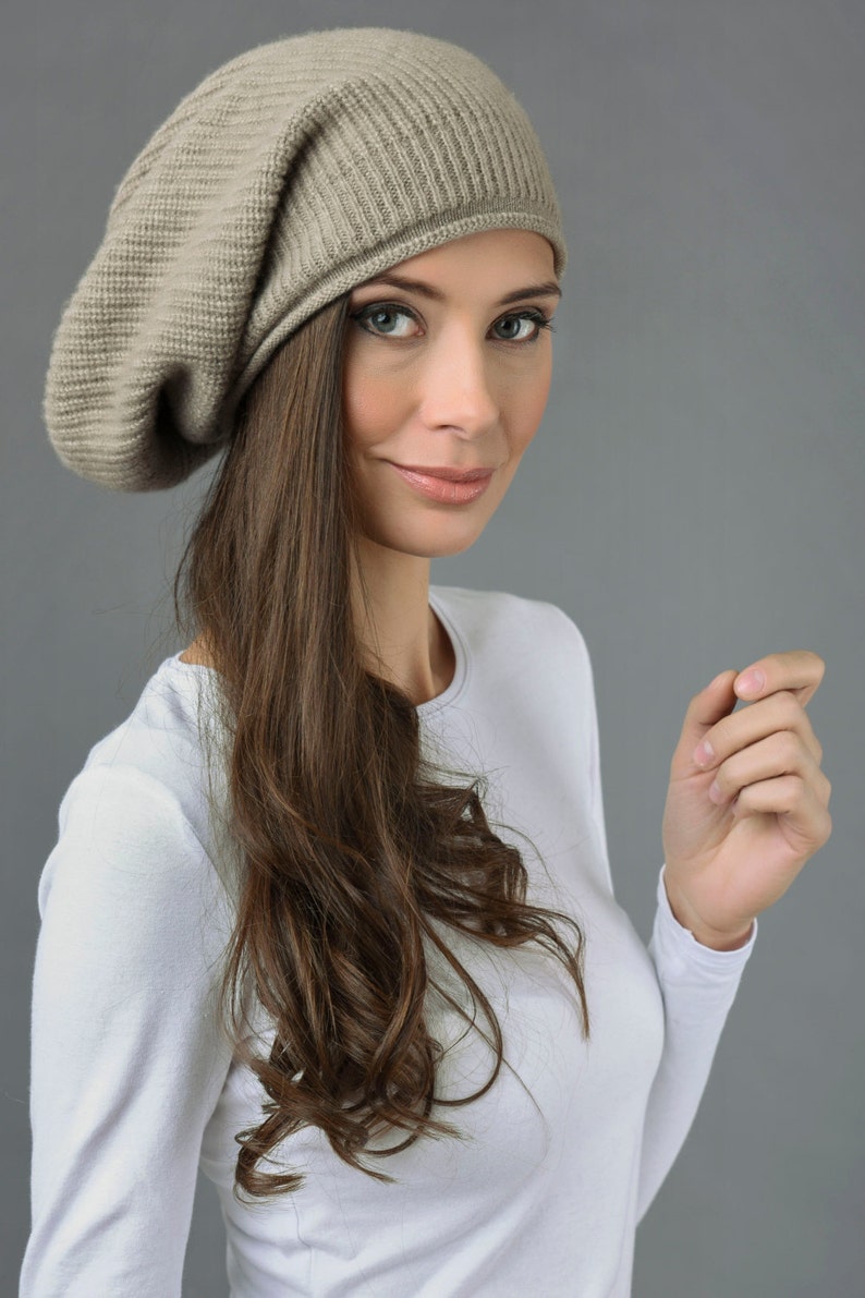May include: A woman with long brown hair is wearing a light brown slouchy beanie hat and a white long-sleeved shirt.