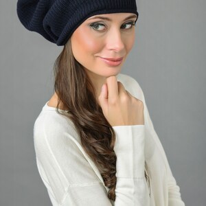 May include: A woman wearing a dark blue slouchy beanie hat with a white sweater.