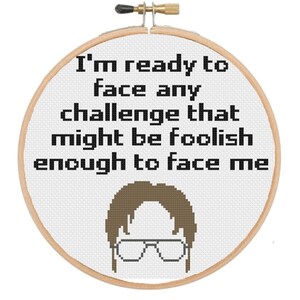 May include: A white embroidery hoop with a brown background and black text that reads "I'm ready to face any challenge that might be foolish enough to face me". A brown cartoon image of a man with glasses is below the text.