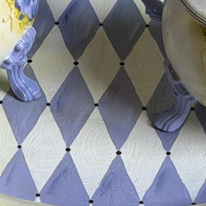 Puede incluir: Una superficie con un patr&oacute;n repetitivo de rombos de arlequ&iacute;n en tonos alternos de morado claro y blanco hueso. Peque&ntilde;os puntos negros se sit&uacute;an en cada intersecci&oacute;n de los rombos. La superficie presenta una sutil textura de remolinos.