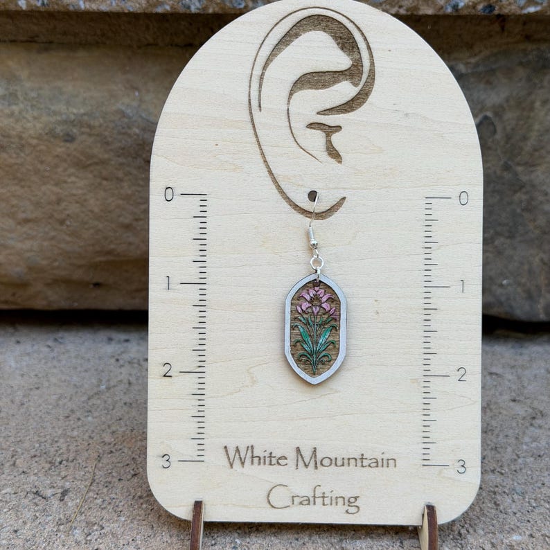 K&ouml;nnte beinhalten: Ein einzelner Ohrh&auml;nger mit einem spitz zulaufenden, ovalen Holzanh&auml;nger mit einem Blumenmotiv in Rosa und Gr&uuml;n. Der Ohrring h&auml;ngt an einem silberfarbenen Haken auf einer hellen Holz-Displaykarte mit einem 3-Zoll-Lineal und dem Text White Mountain Crafting.