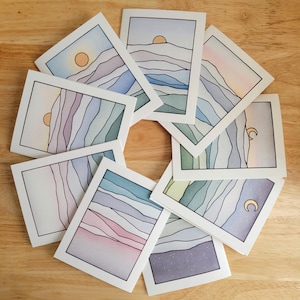 Può includere: Set di otto carte acquerello che rappresentano un paesaggio stilizzato con montagne, un sole e una luna. Le carte sono tutte di colori diversi e hanno un aspetto dipinto a mano.