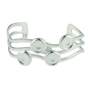 May include: Silver bracelet with four round, clear, glass cabochon settings. The bracelet has a wavy design and is made of three bands.