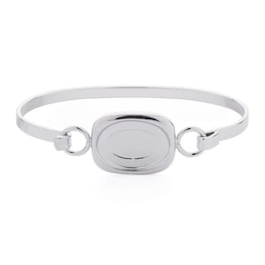 May include: A silver bangle bracelet with a rectangular charm featuring an oval shape in the centre. The charm has a smooth, polished finish.