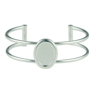Puede incluir: Un brazalete de doble banda de plata con un dije ovalado en blanco en el centro.