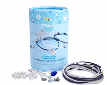 May include: A blue and white cylindrical box with the text "Pipkits Snow Days Friendship Charm Bracelet Kit Make 6 bracelets for you & your friends" on the front. The box contains a variety of silver charms, beads, and strings for making friendship bracelets.