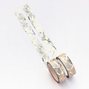 K&ouml;nnte beinhalten: Zwei Rollen Washi-Tape mit Marmor- und Goldmuster. Das Band ist wei&szlig; mit goldenen Linien und einem Marmoreffekt.