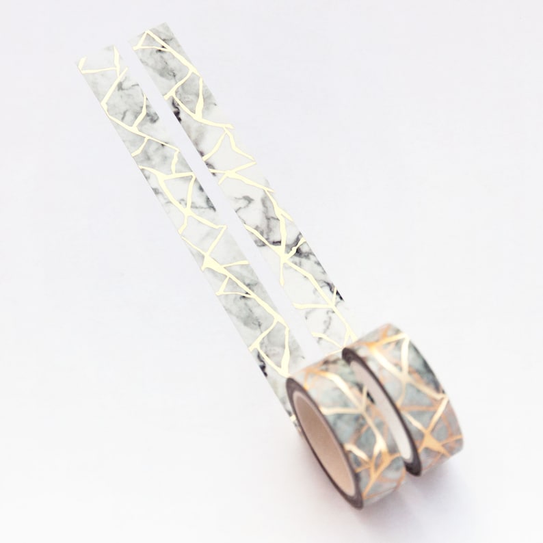 K&ouml;nnte beinhalten: Zwei Rollen Washi-Tape mit Marmor- und Goldmuster. Das Band ist wei&szlig; mit goldenen Linien und einem Marmoreffekt.