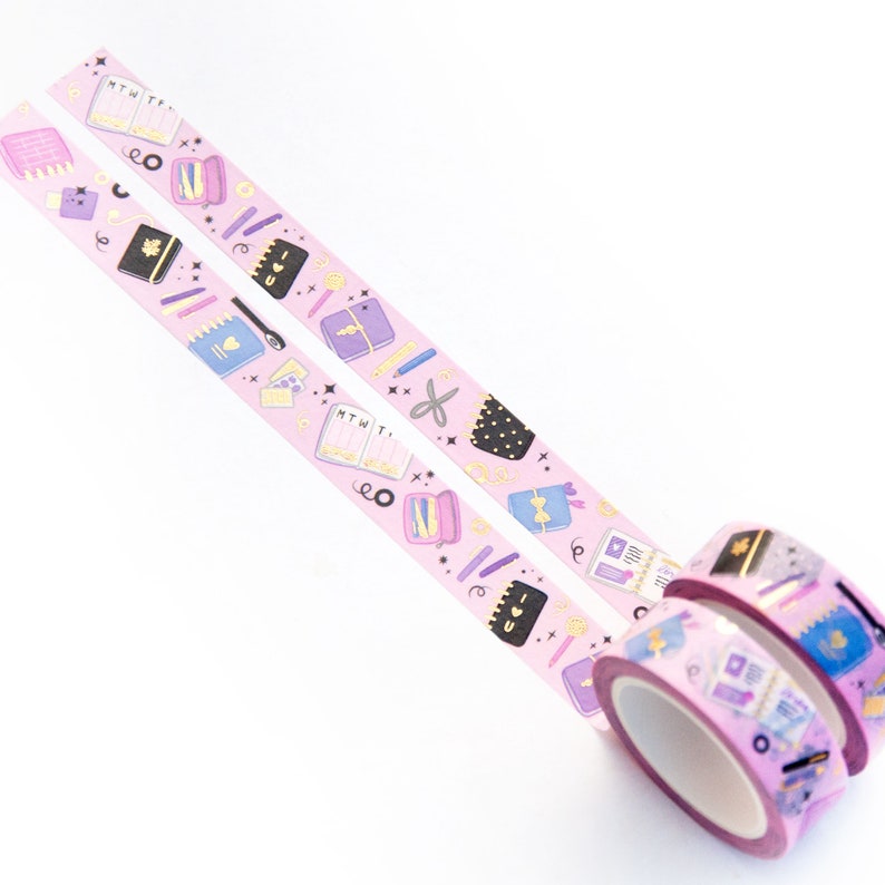 May include: Two rolls of pink washi tape with a gold glitter design. The tape features a repeating pattern of black and purple illustrated notebooks, pens, pencils, scissors, and other stationery items. The tape also includes the text "MTWThF" and "I love you".