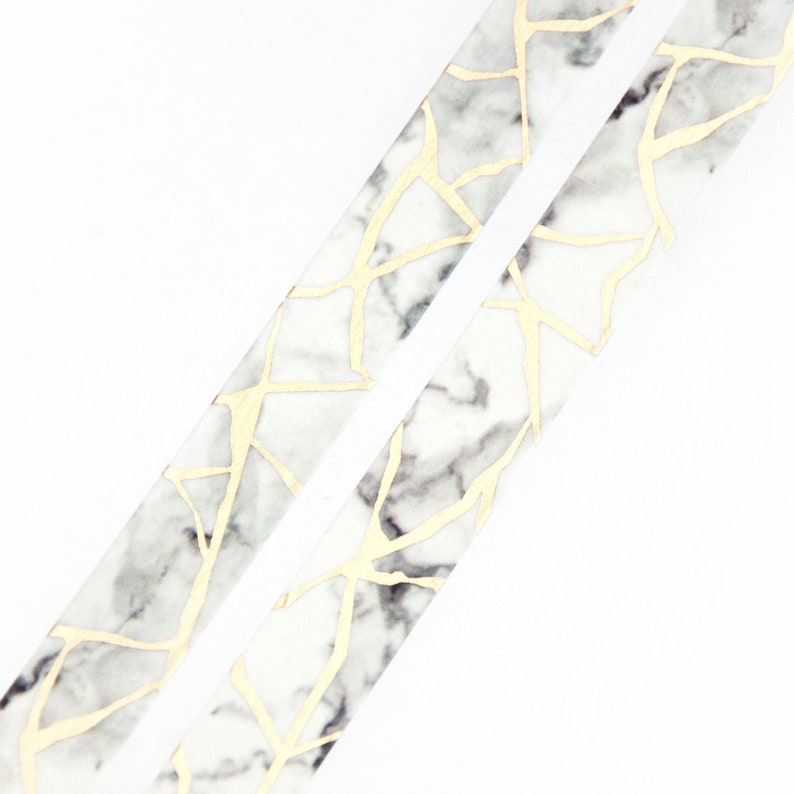 K&ouml;nnte beinhalten: Zwei Rollen wei&szlig;es und goldenes Washi-Tape mit Marmormuster. Das Band hat ein geometrisches Muster aus goldenen Linien auf wei&szlig;em Hintergrund mit grauen Marmorakzenten.