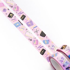 May include: Two rolls of pink washi tape with a gold glitter background and a repeating pattern of colorful illustrations of notebooks, pens, pencils, scissors, and other stationery items. The text "MTWT" and "I love you" are visible on the tape.