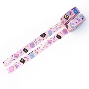 May include: Two rolls of pink washi tape with a gold and purple pattern of notebooks, pens, and other stationery items. The tape is on a white background.