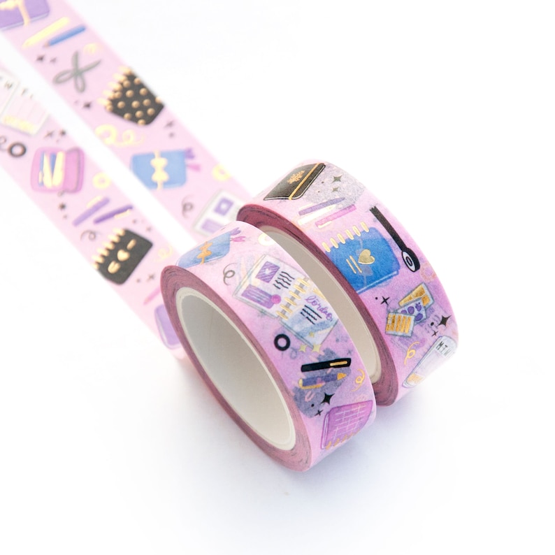 May include: Two rolls of pink washi tape with gold accents. The tape features a pattern of books, pens, and other stationery items. The tape is perfect for adding a touch of whimsy to your planner or journal.
