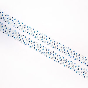 May include: Two rolls of white washi tape with a repeating pattern of blue and silver raindrops.