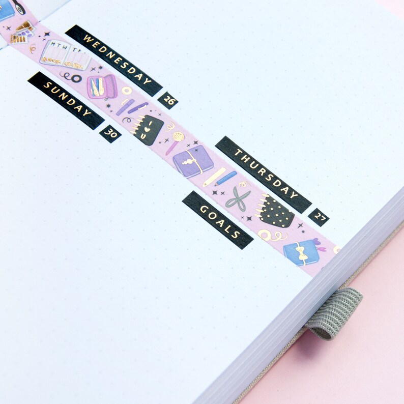 May include: A pink and purple washi tape with a pattern of stars, scissors, pencils, and other stationery items. The tape is labeled "SUNDAY 30", "WEDNESDAY 26", "THURSDAY 27", and "GOALS".