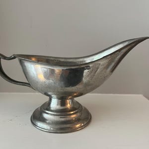 May include: A silver gravy boat with a handle and a pedestal base.