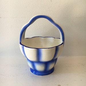 May include: A small white ceramic basket with a blue and white checkered pattern and a blue handle.
