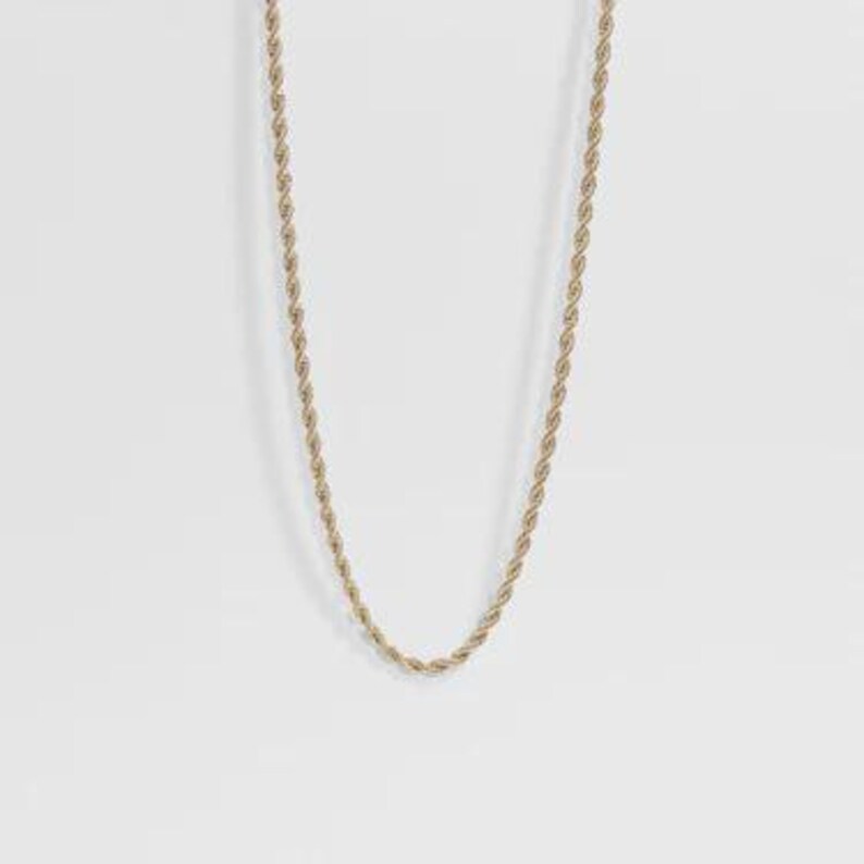 May include: A gold-toned rope chain necklace featuring a twisted, spiraling metal link design. The chain is displayed in a simple U-shape, showcasing the uniform texture and metallic finish of the interconnected links throughout the entire length.