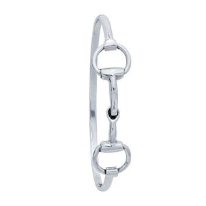 Könnte beinhalten: Ein silbernes Armreif-Armband mit einem Doppel-Trense-Design. Das Armband ist aus poliertem Metall gefertigt und hat einen schlichten, eleganten Look.