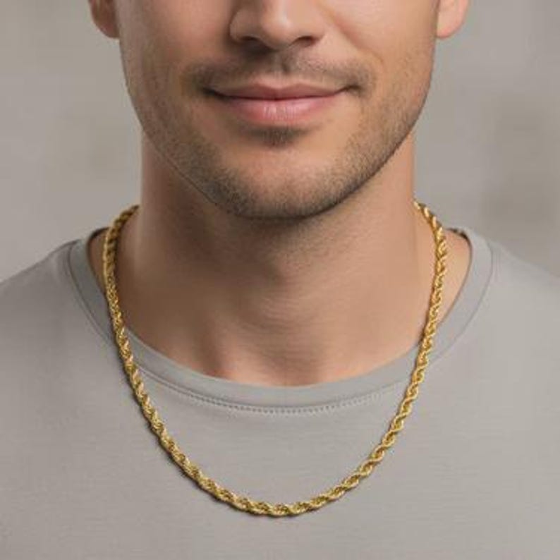 May include: A gold-colored rope chain necklace. The chain is draped around a person's neck, resting on a gray t-shirt. The chain has a twisted rope design.