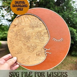 May include: A digital download SVG file for laser cutting a crescent moon with a floral pattern. The moon is orange and the floral pattern is on a natural wood background. The text "SVG FILE FOR LASERS" and "THIS LISTING IS NOT FOR A PHYSICAL PRODUCT" is at the bottom of the image.