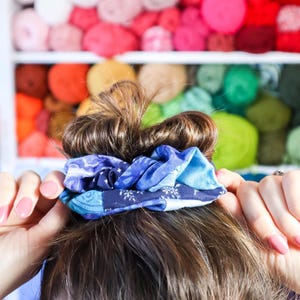 K&ouml;nnte beinhalten: Ein blaues und wei&szlig;es Stoffscrunchie, das das braune Haar einer Frau in einem Dutt h&auml;lt.
