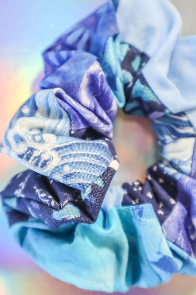 K&ouml;nnte beinhalten: Ein blauer und wei&szlig;er gemusterter Haargummi aus Stoff. Der Haargummi besteht aus mehreren zusammengen&auml;hten Stoffteilen.