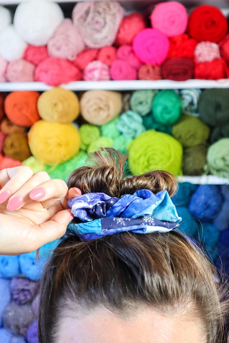 K&ouml;nnte beinhalten: Nahaufnahme von Haaren, die mit einem blauen und wei&szlig;en gemusterten Haargummi zu einem Dutt gebunden sind. Der Hintergrund ist eine Wand mit bunten Wollkn&auml;ueln.
