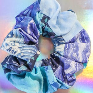 K&ouml;nnte beinhalten: Ein blauer und wei&szlig;er gemusterter Haargummi aus Stoffresten. Der Haargummi besteht aus verschiedenen Stoffen mit verschiedenen blauen und wei&szlig;en Mustern.