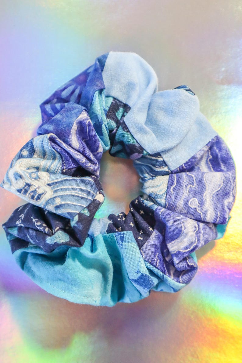 K&ouml;nnte beinhalten: Ein blauer und wei&szlig;er gemusterter Haargummi aus Stoffresten. Der Haargummi besteht aus verschiedenen Stoffen mit verschiedenen blauen und wei&szlig;en Mustern.