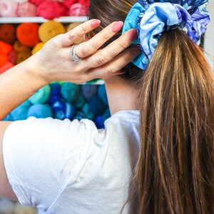 K&ouml;nnte beinhalten: Eine Frau mit langen braunen Haaren, die ein blaues und wei&szlig; gemustertes Haargummi im Haar tr&auml;gt. Das Haargummi ist um einen Pferdeschwanz gebunden.