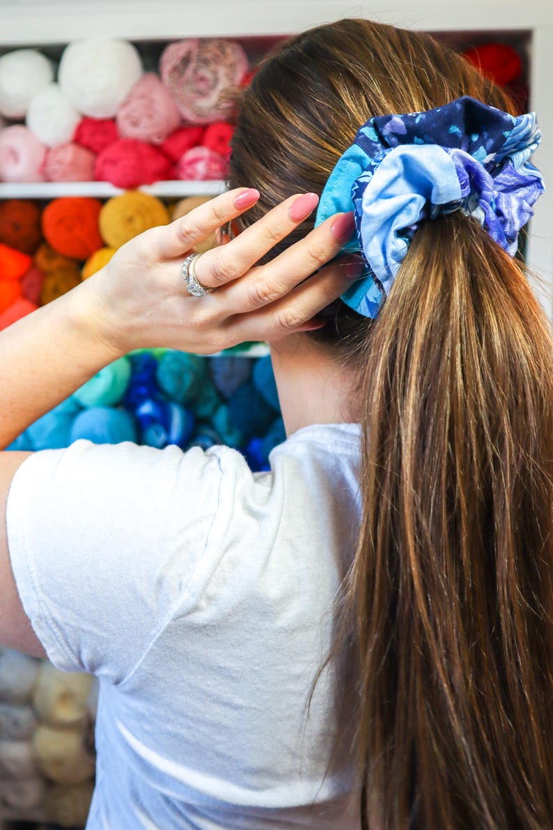 K&ouml;nnte beinhalten: Eine Frau mit langen braunen Haaren, die ein blaues und wei&szlig; gemustertes Haargummi im Haar tr&auml;gt. Das Haargummi ist um einen Pferdeschwanz gebunden.