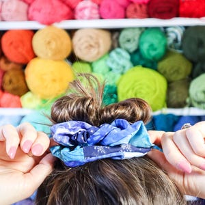 K&ouml;nnte beinhalten: Ein blaues und wei&szlig;es gemustertes Haargummi h&auml;lt das braune Haar einer Frau in einem Dutt.