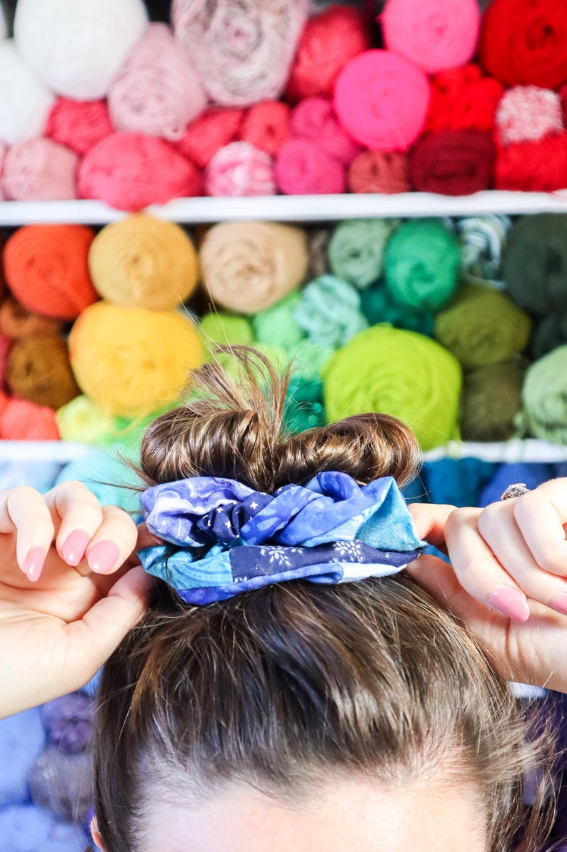 K&ouml;nnte beinhalten: Ein blaues und wei&szlig;es gemustertes Haargummi h&auml;lt das braune Haar einer Frau in einem Dutt.