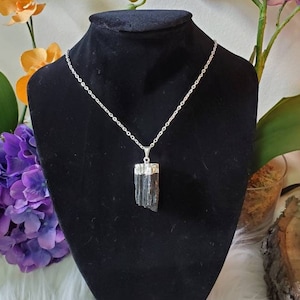 Puede incluir: Un collar de cadena de plata con un colgante de turmalina negra. El colgante es una pieza bruta de turmalina negra sin pulir con una tapa de plata en la parte superior.