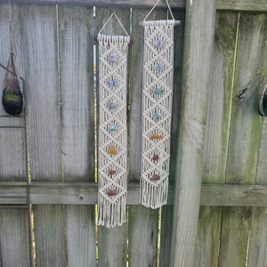 May include: Two macrame wall hangings with crystals. Each hanging features a white macrame design with a variety of colored crystals.