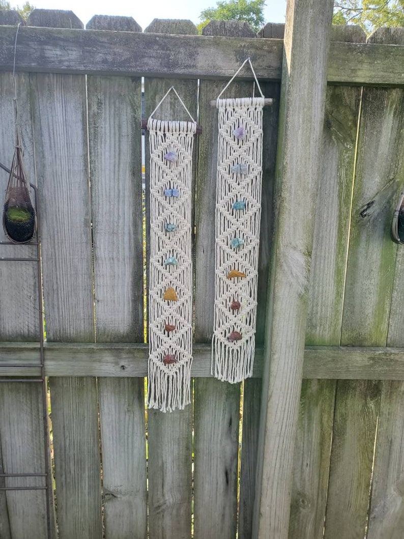 May include: Two macrame wall hangings with crystals. Each hanging features a white macrame design with a variety of colored crystals.