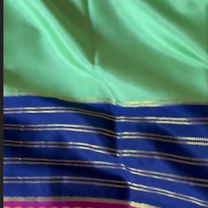 May include: A light green fabric with a blue and pink border. The blue section has horizontal gold stripes. The pink border has a gold dotted pattern. The fabric has a shiny, smooth texture.