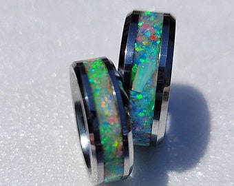 May include: Two silver rings with a band of iridescent opal. The opal is a mix of green, blue, and white.