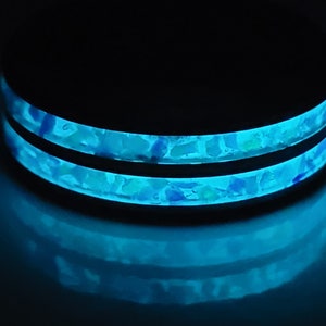 May include: A black ring with two bands of blue and white speckled resin. The resin glows in the dark.