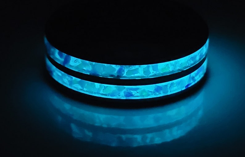 May include: A black ring with two bands of blue and white speckled resin. The resin glows in the dark.