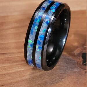 May include: A black tungsten carbide ring with two inlaid bands of blue and white opal.