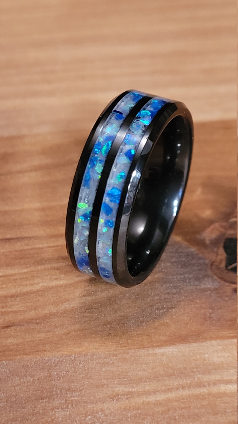 May include: A black tungsten carbide ring with two inlaid bands of blue and white opal.