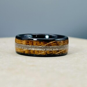 May include: A black and brown ring with a wood inlay. The ring has a polished finish and a thin white line running around the edge.
