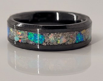 May include: A black tungsten carbide ring with a band of iridescent opal and other stones set in a black resin.