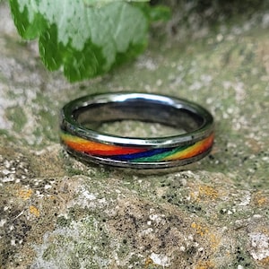Könnte beinhalten: Ein silberner Ring mit einem Regenbogen-Inlay. Der Ring liegt auf einer strukturierten Steinoberfläche.