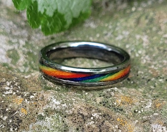 May include: A silver ring with a rainbow inlay. The ring is on a textured rock surface.