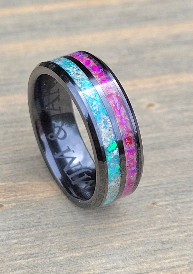 May include: Black tungsten carbide ring with a pink and blue opal inlay. The ring is engraved with the words "My & Jay".