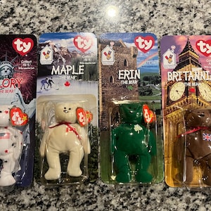 May include: Four Ty Beanie Baby plush toys in their original packaging. The toys are named Glory, Maple, Erin, and Britannia. Each toy is wearing a different outfit representing a different country. Glory is wearing a red, white, and blue outfit with stars. Maple is wearing a white outfit with a Canadian flag patch. Erin is wearing a green outfit with a shamrock patch. Britannia is wearing a brown outfit with a Union Jack patch.